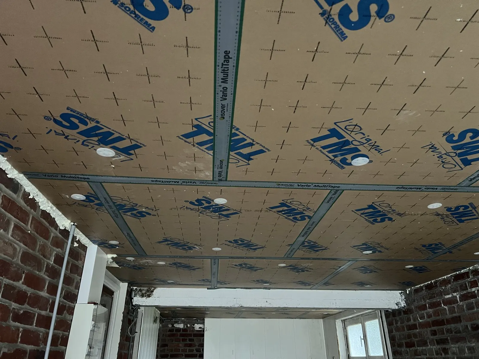 sous-face du plancher bas isolée à Faumont : panneaux TMS fixés par rosaces, joints Vario MultiTape, mur en brique